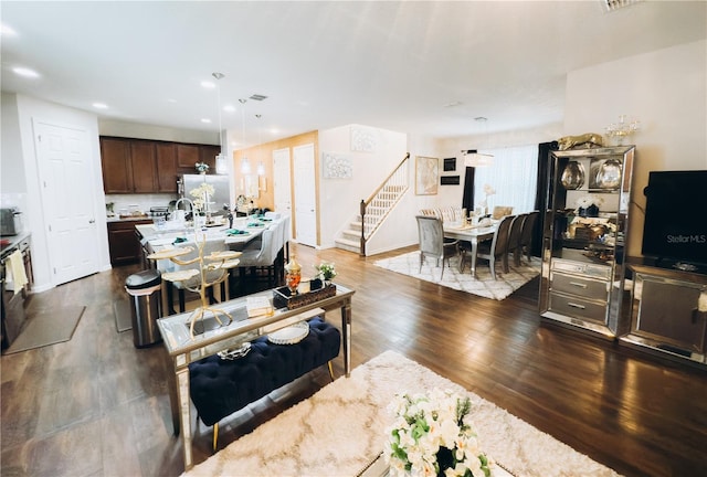 kitchen featuring light stone countertops, stainless steel fridge, dark brown cabinetry, pendant lighting, and dark wood-type flooring