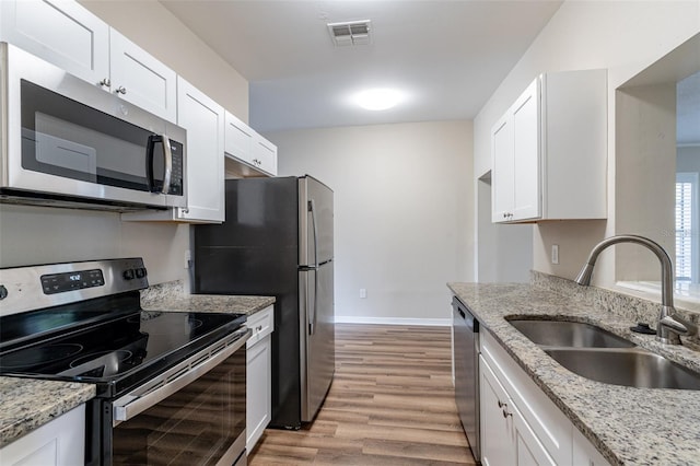 kitchen with stainless steel appliances, white cabinetry, light stone countertops, sink, and light hardwood / wood-style flooring