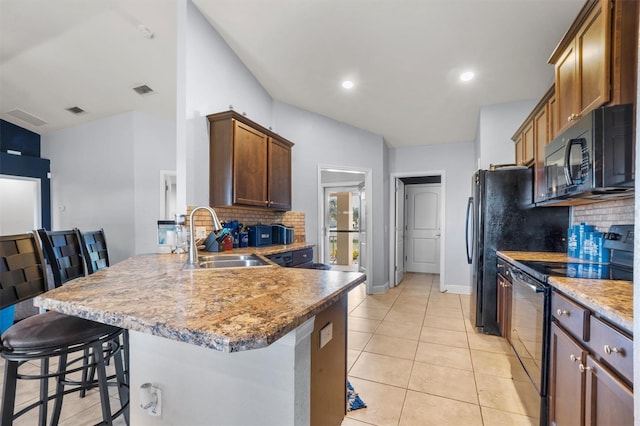 kitchen featuring tasteful backsplash, black appliances, sink, kitchen peninsula, and a breakfast bar