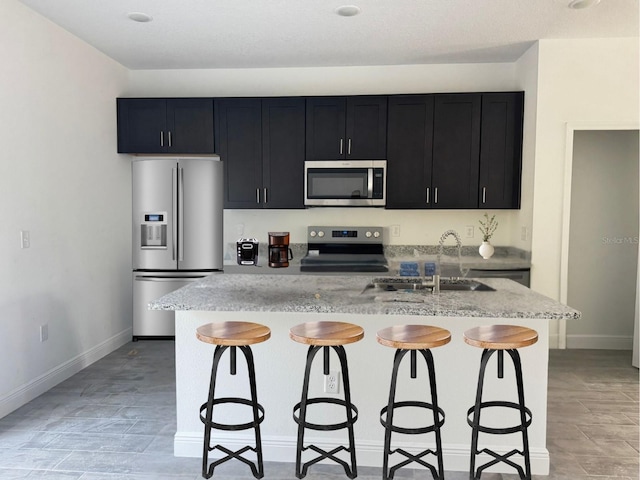 kitchen featuring a kitchen island with sink, sink, a breakfast bar area, light stone countertops, and stainless steel appliances