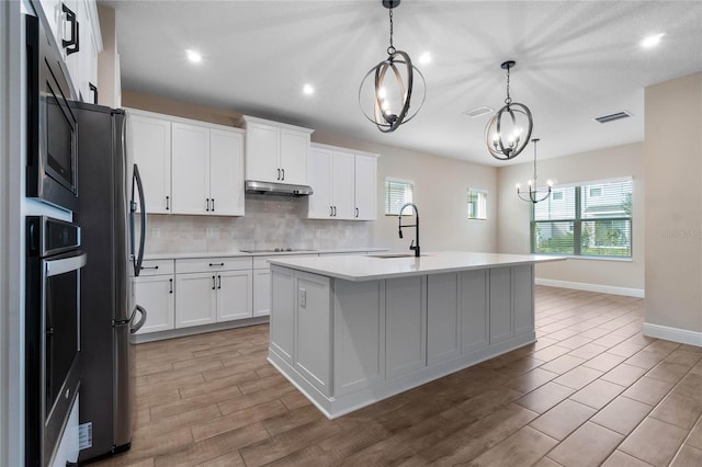 kitchen featuring under cabinet range hood, a sink, visible vents, light countertops, and tasteful backsplash