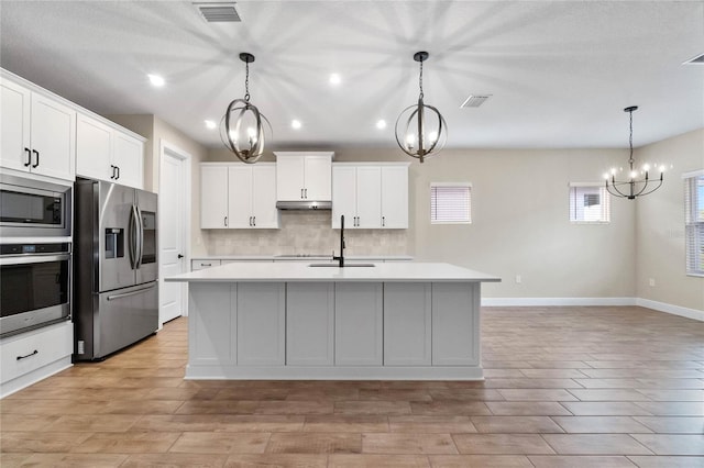 kitchen with a kitchen island with sink, decorative light fixtures, and appliances with stainless steel finishes