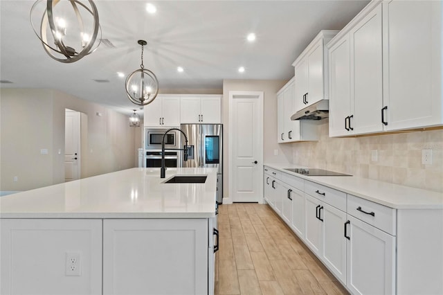 kitchen featuring under cabinet range hood, white cabinetry, appliances with stainless steel finishes, tasteful backsplash, and an island with sink