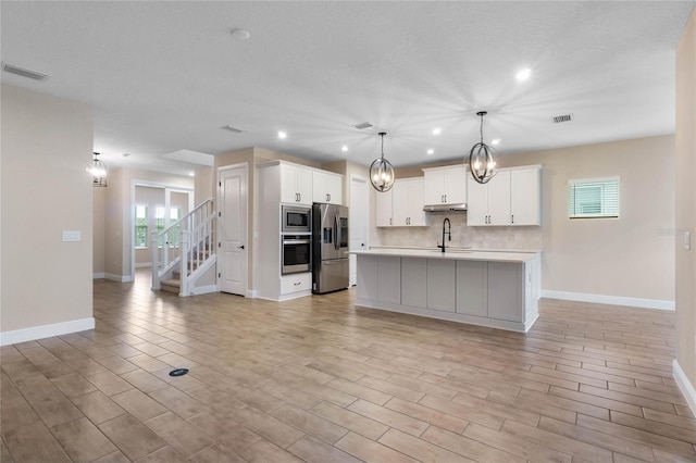 kitchen featuring stainless steel appliances, sink, a center island with sink, white cabinetry, and hanging light fixtures