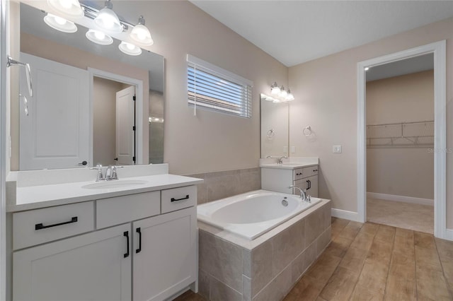 bathroom with wood-type flooring, vanity, and tiled tub