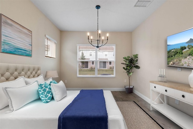 bedroom featuring a chandelier, visible vents, baseboards, and wood finished floors