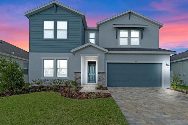 view of front facade featuring decorative driveway, stucco siding, a lawn, a garage, and stone siding