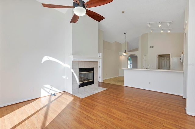 unfurnished living room with high vaulted ceiling, wood-type flooring, a tile fireplace, and ceiling fan