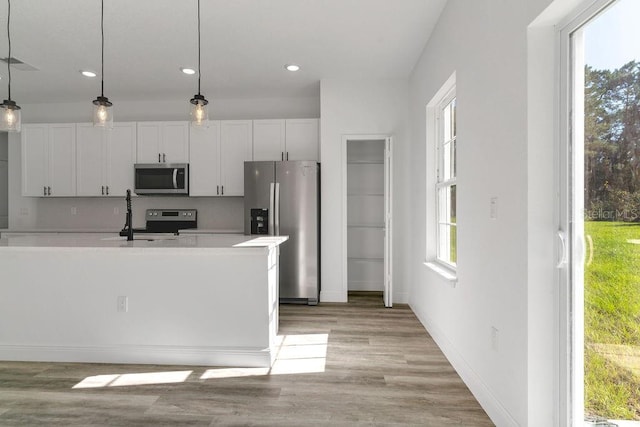 kitchen featuring appliances with stainless steel finishes, sink, white cabinetry, light hardwood / wood-style floors, and decorative light fixtures