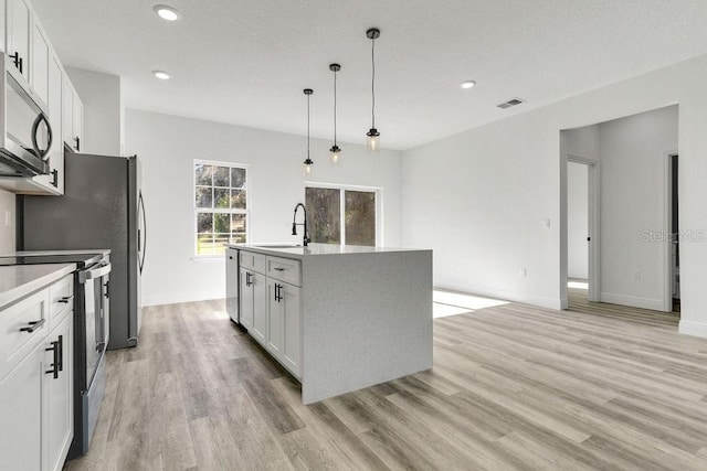 kitchen featuring appliances with stainless steel finishes, an island with sink, hanging light fixtures, light hardwood / wood-style floors, and white cabinets