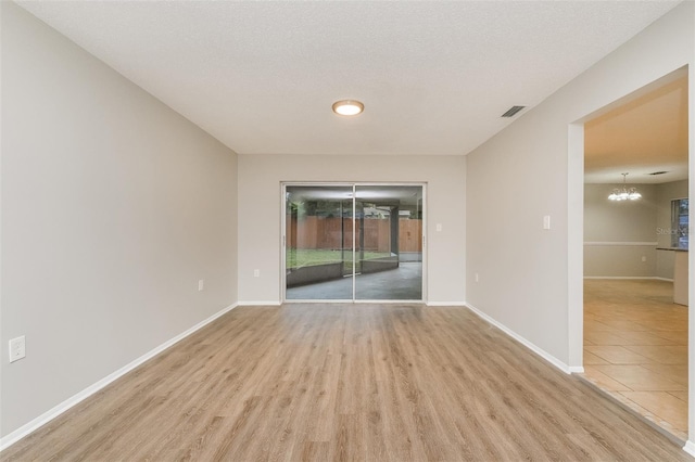 empty room featuring a notable chandelier, a textured ceiling, and light hardwood / wood-style flooring