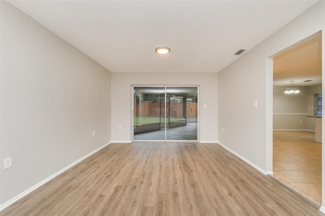 empty room featuring an inviting chandelier, wood finished floors, visible vents, and baseboards