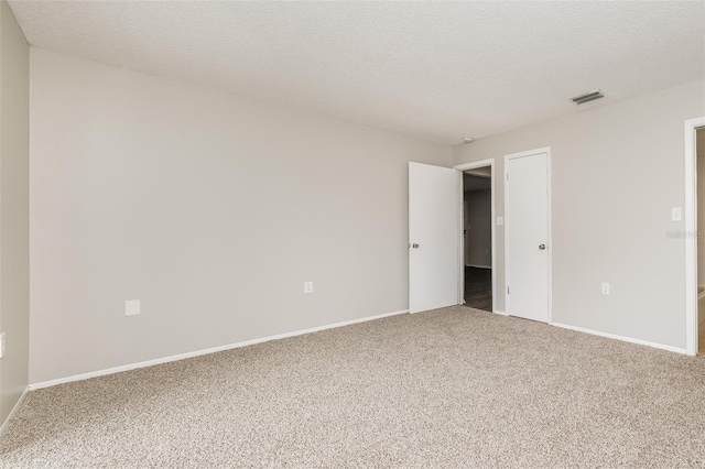 carpeted spare room featuring a textured ceiling, visible vents, and baseboards