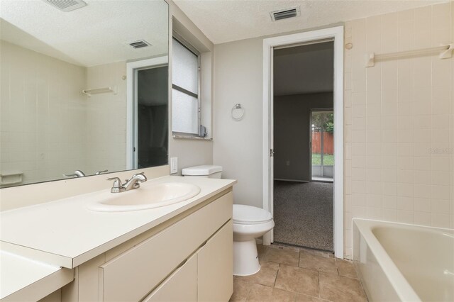 full bathroom with tiled shower / bath, a textured ceiling, toilet, vanity, and tile patterned floors