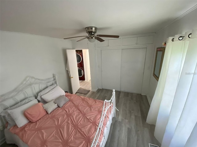 bedroom featuring ceiling fan, light wood-type flooring, ornamental molding, stacked washer and dryer, and a closet