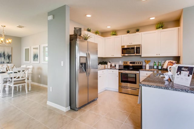 kitchen featuring appliances with stainless steel finishes, white cabinetry, decorative light fixtures, dark stone countertops, and light tile patterned floors