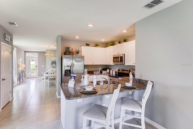 kitchen featuring a kitchen breakfast bar, dark stone counters, white cabinetry, an inviting chandelier, and appliances with stainless steel finishes