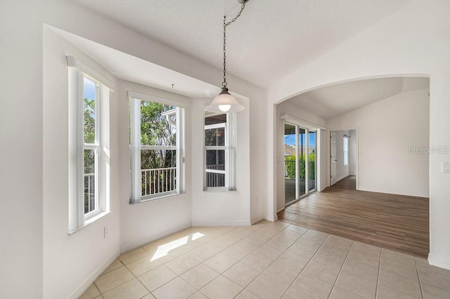 unfurnished dining area featuring vaulted ceiling, a textured ceiling, and light hardwood / wood-style flooring