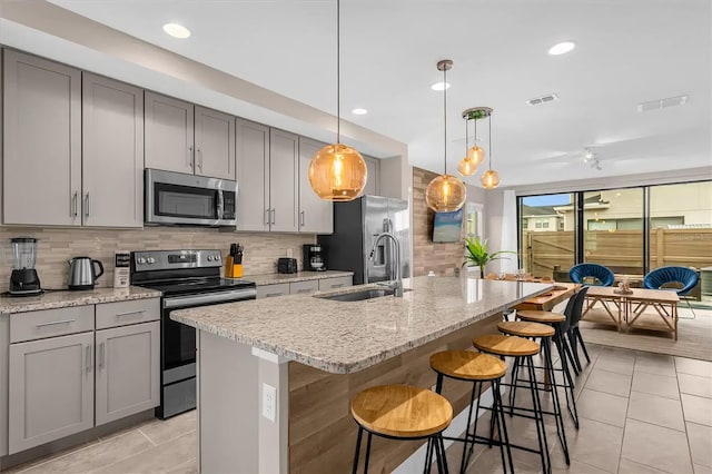 kitchen with appliances with stainless steel finishes, hanging light fixtures, a center island with sink, and gray cabinetry