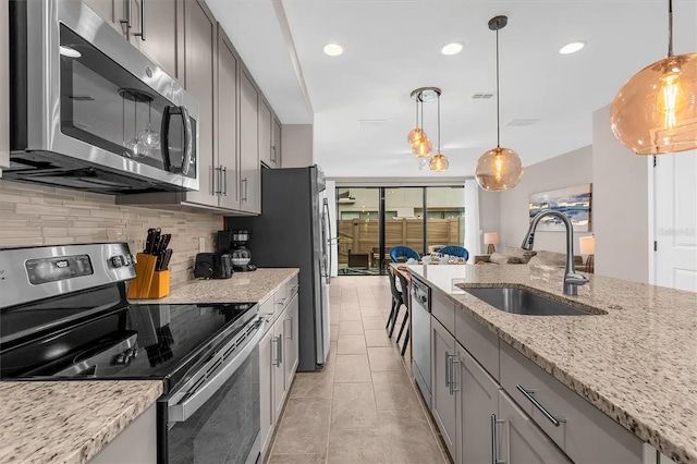 kitchen featuring decorative light fixtures, stainless steel appliances, sink, and light stone counters