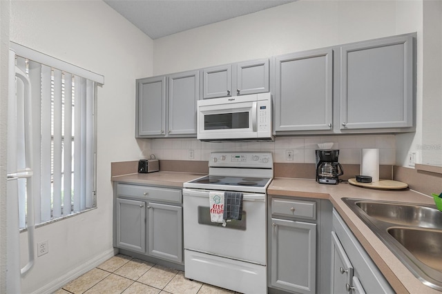 kitchen featuring decorative backsplash, sink, light tile patterned floors, gray cabinets, and white appliances