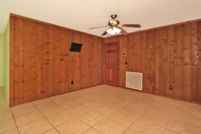 tiled empty room featuring ceiling fan, a textured ceiling, and wood walls