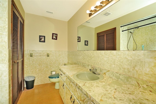 bathroom with toilet, vanity, a tile shower, and tile walls