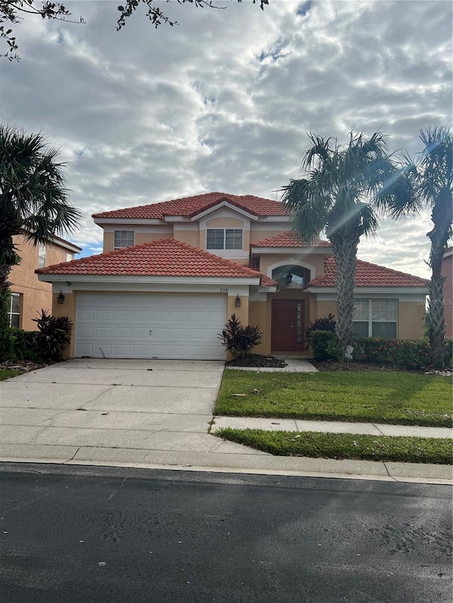 mediterranean / spanish-style home with stucco siding, a tiled roof, a front yard, concrete driveway, and an attached garage