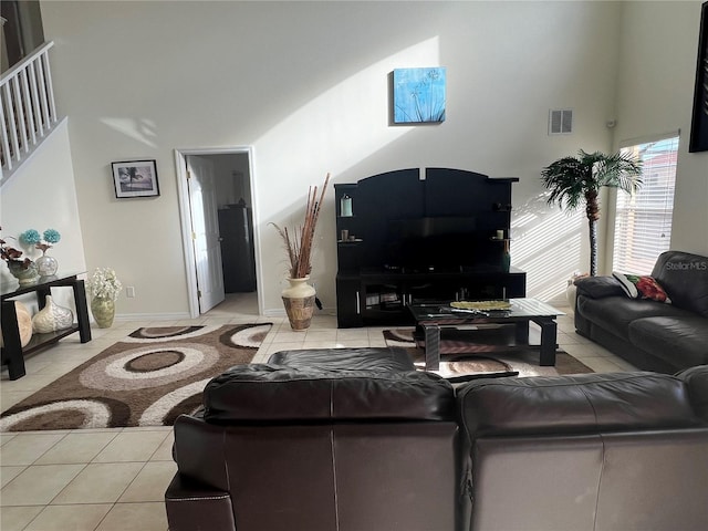 living area featuring baseboards, visible vents, light tile patterned floors, and a towering ceiling