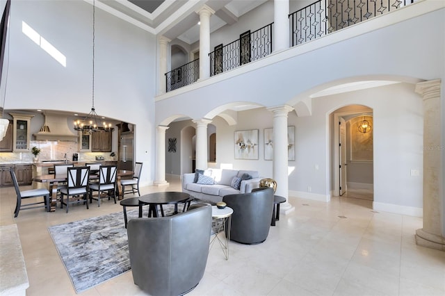 living room with a high ceiling, ornate columns, ornamental molding, light tile patterned flooring, and an inviting chandelier