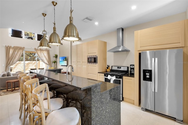 kitchen with appliances with stainless steel finishes, an island with sink, wall chimney exhaust hood, decorative light fixtures, and light tile patterned floors