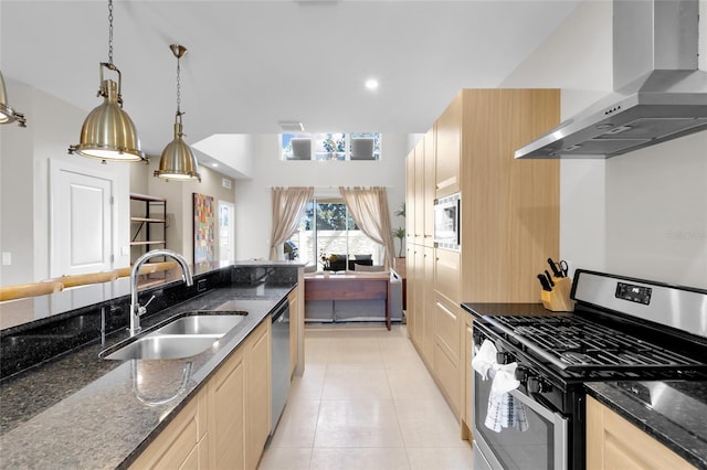 kitchen featuring wall chimney range hood, appliances with stainless steel finishes, dark stone countertops, sink, and decorative light fixtures