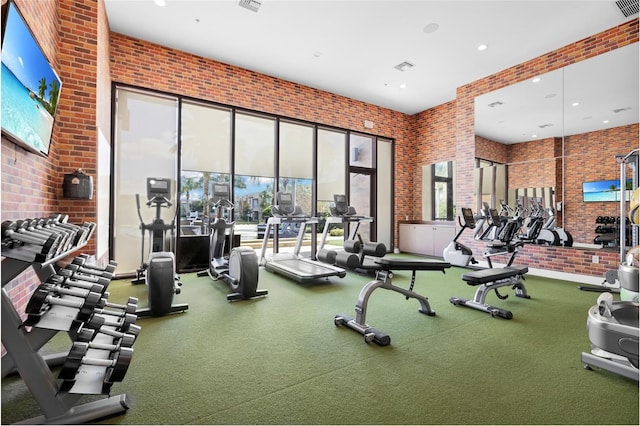 gym featuring a healthy amount of sunlight, brick wall, and a high ceiling