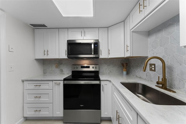 kitchen featuring sink, appliances with stainless steel finishes, tasteful backsplash, light stone counters, and white cabinetry