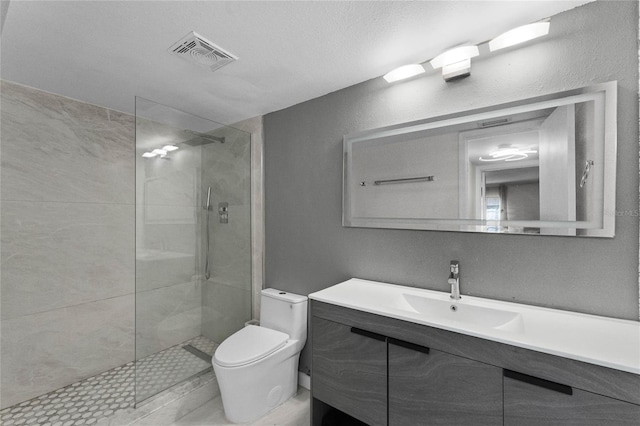 bathroom with a tile shower, vanity, a textured ceiling, and toilet