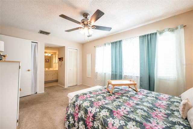 bedroom featuring a textured ceiling, ensuite bathroom, ceiling fan, and light colored carpet