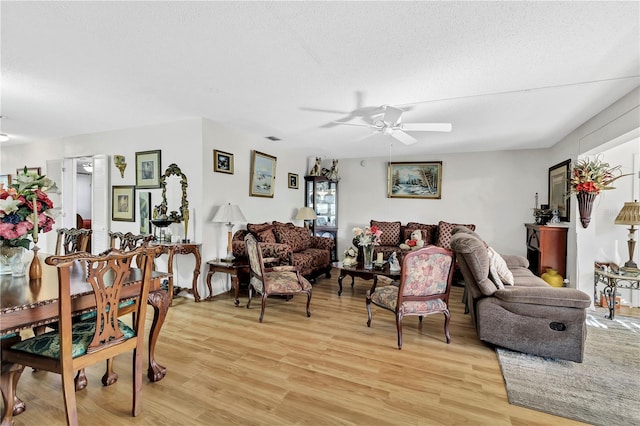 living room with ceiling fan, a textured ceiling, and light wood-type flooring