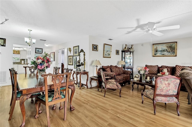 dining room with light hardwood / wood-style floors, a textured ceiling, and ceiling fan with notable chandelier