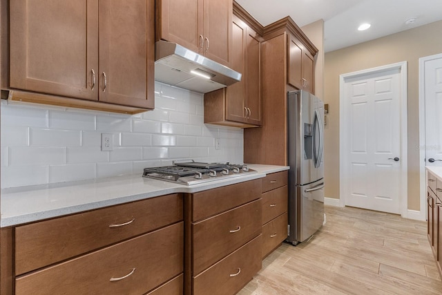 kitchen featuring light stone countertops, light wood-type flooring, stainless steel appliances, and tasteful backsplash