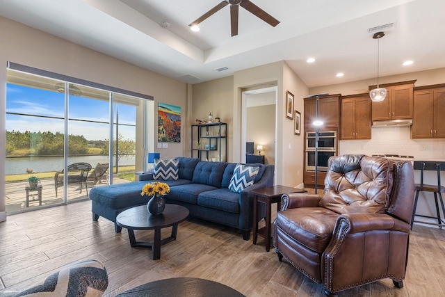 living room featuring ceiling fan, a water view, and light wood-type flooring