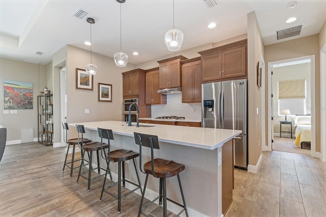 kitchen featuring light wood-type flooring, stainless steel appliances, hanging light fixtures, and a breakfast bar area