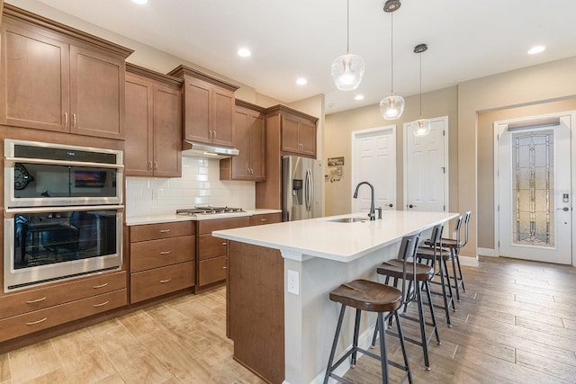 kitchen featuring a breakfast bar, stainless steel appliances, decorative light fixtures, light hardwood / wood-style flooring, and an island with sink