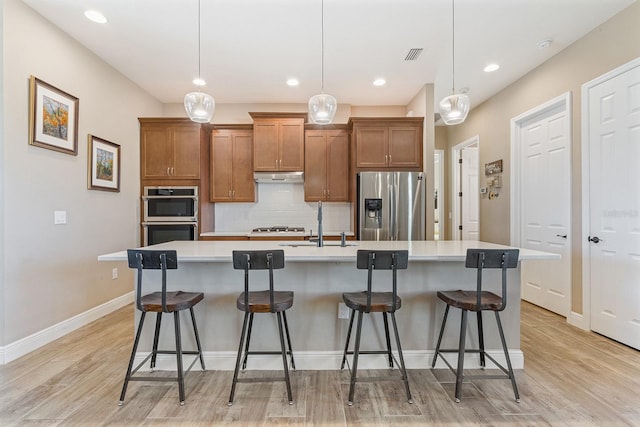 kitchen featuring hanging light fixtures, stainless steel appliances, an island with sink, a breakfast bar, and light wood-type flooring