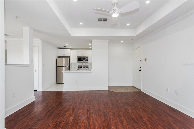 unfurnished living room featuring a raised ceiling, ceiling fan, wood-type flooring, and ornamental molding