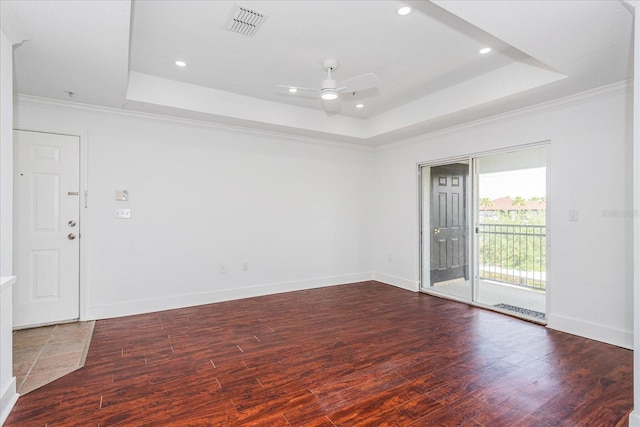 spare room featuring a raised ceiling, ceiling fan, crown molding, and dark wood-type flooring