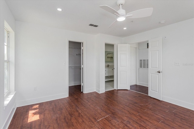 unfurnished bedroom with a walk in closet, ceiling fan, a closet, and dark wood-type flooring