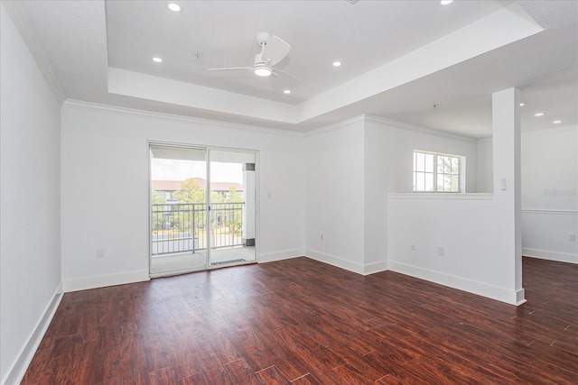 empty room with a raised ceiling, crown molding, dark wood-type flooring, and a healthy amount of sunlight