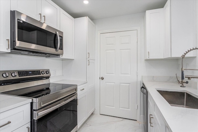 kitchen with white cabinets, stainless steel appliances, light stone counters, and sink