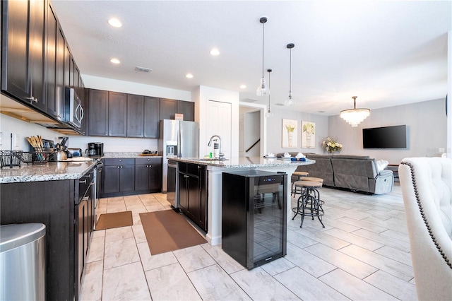 kitchen featuring dark brown cabinets, a kitchen island with sink, a kitchen bar, decorative light fixtures, and sink