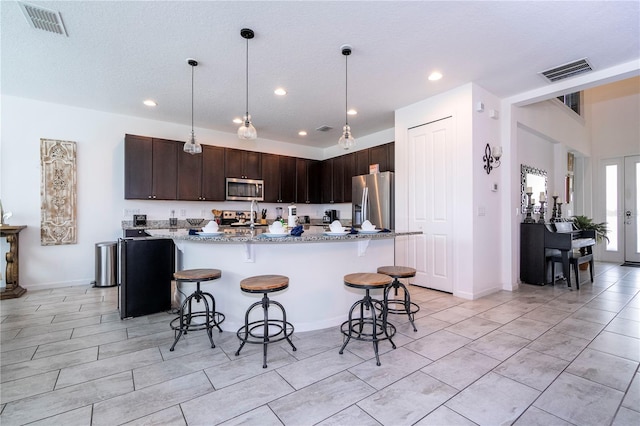 kitchen with a breakfast bar area, hanging light fixtures, stainless steel appliances, dark brown cabinetry, and light stone counters